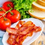 Crispy air fryer bacon on a white plate with lettuce, tomato, and bread for a BLT.