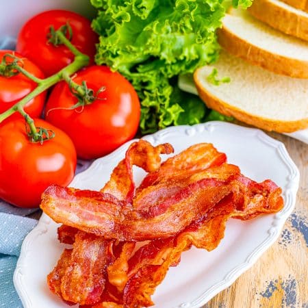 Crispy air fryer bacon on a white plate with lettuce, tomato, and bread for a BLT.