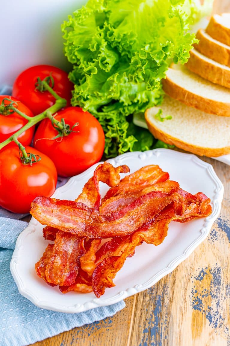 Crispy air fryer bacon on a white plate with lettuce, tomato, and bread for a BLT.