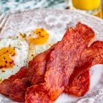 Crispy air fryer turkey bacon on a plate with scrambled eggs and orange juice.