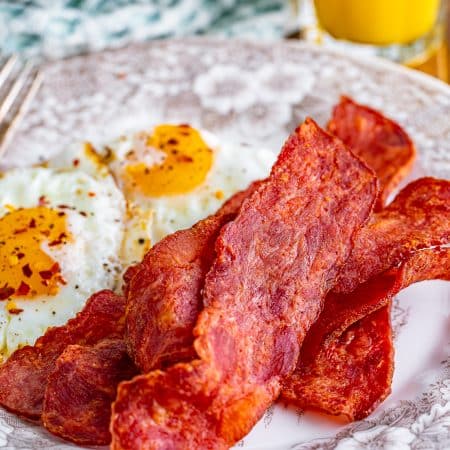 Crispy air fryer turkey bacon on a plate with scrambled eggs and orange juice.