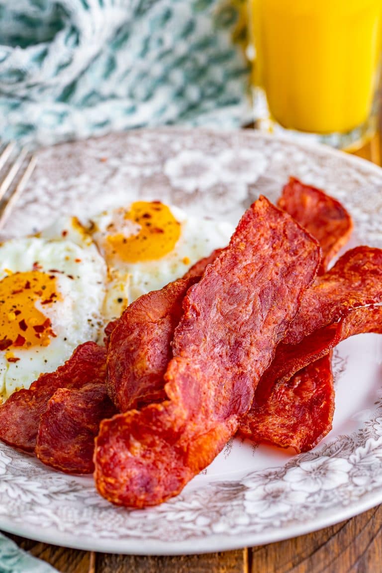 Crispy air fryer turkey bacon on a plate with scrambled eggs and orange juice.