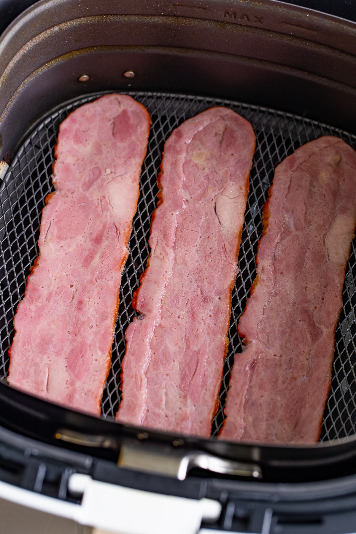 slices of turkey bacon uncooked in an air fryer basket