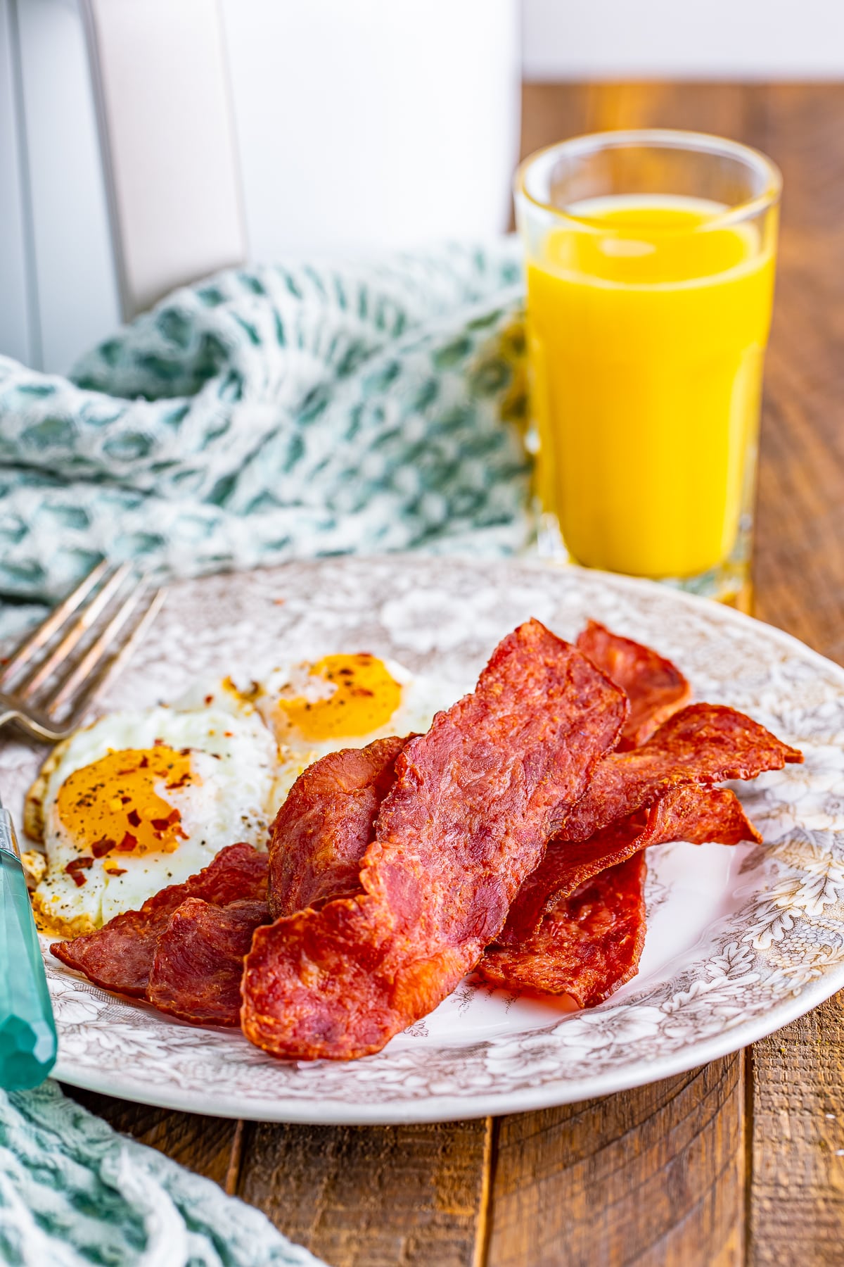 Air fryer turkey bacon on a plate with fried eggs, oj in the background