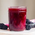 A jar of homemade Blackberry Sauce with fresh blackberries beside it.