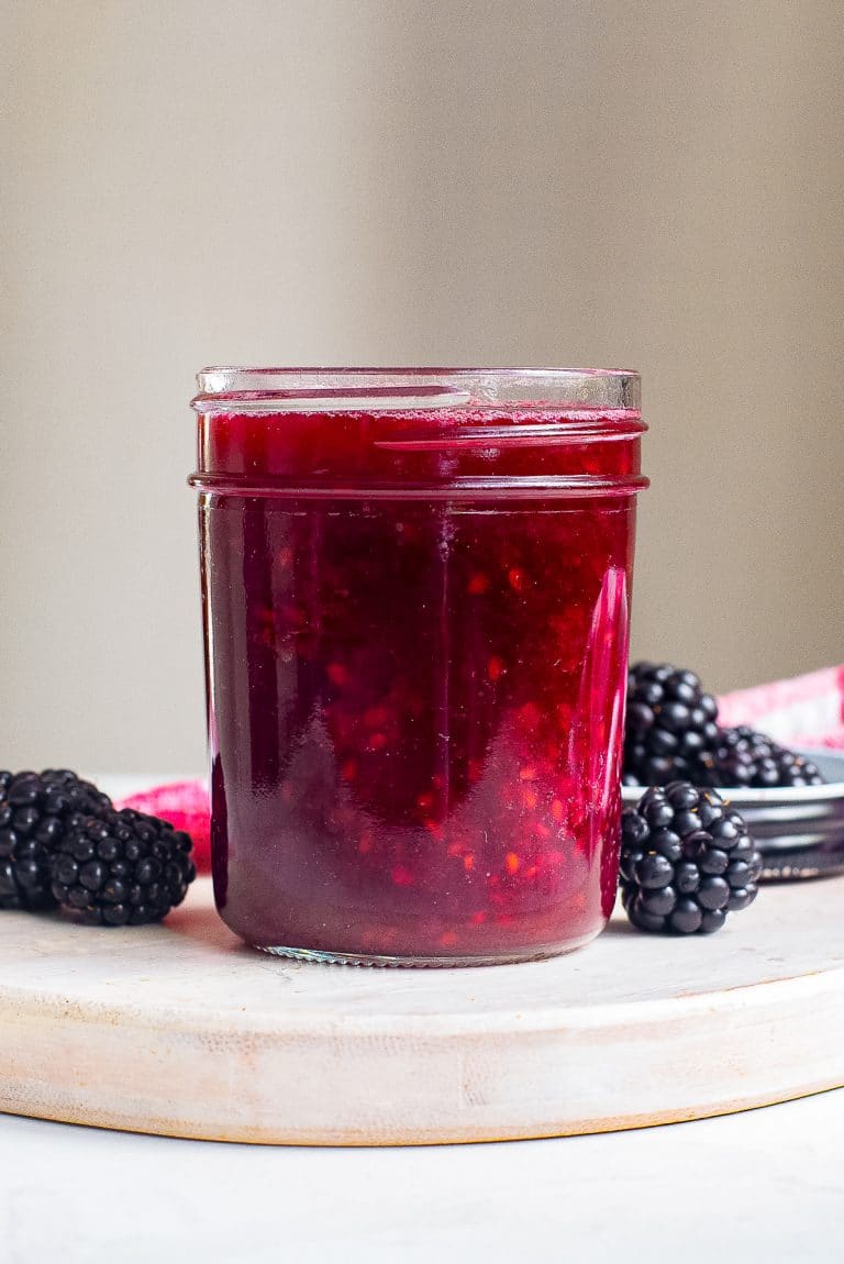 A jar of homemade Blackberry Sauce with fresh blackberries beside it.