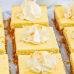 Coconut cheesecake bars topped with whipped cream swirls and toasted coconut arranged on parchment paper.