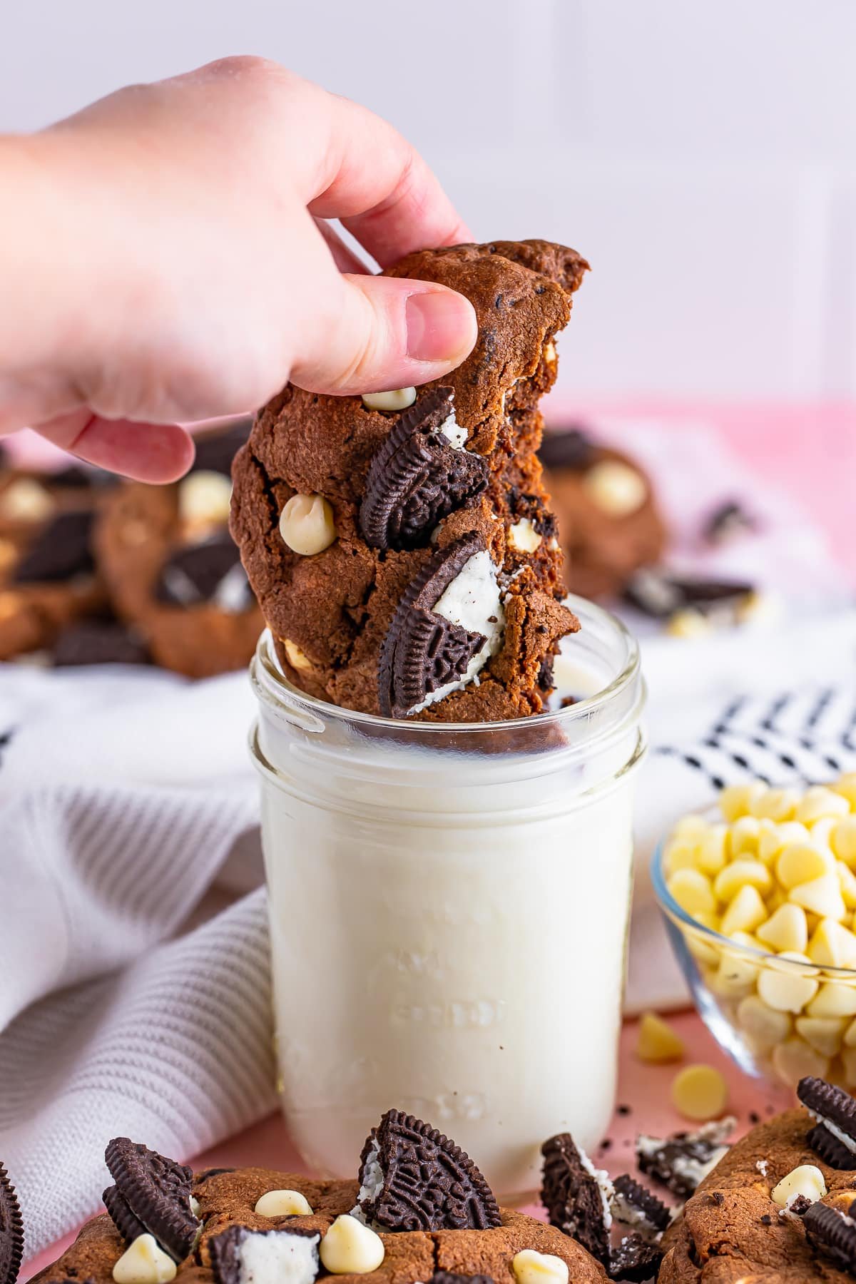 A hand dunking half of a cookies and cream cookie into a glass of milk