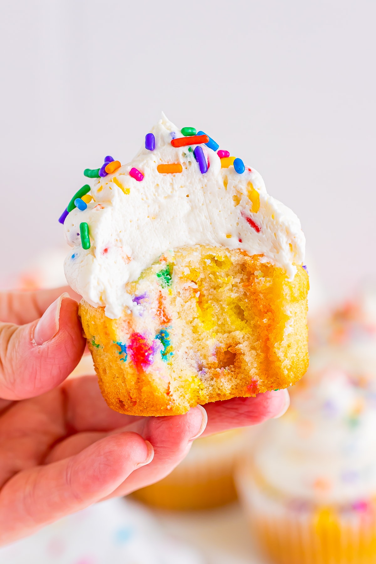 A hand holding a funfetti cupcake with a bite taken out of it in air