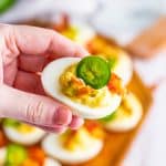 A wood board of jalapeno deviled eggs topped with crispy bacon and fresh jalapeno slices.