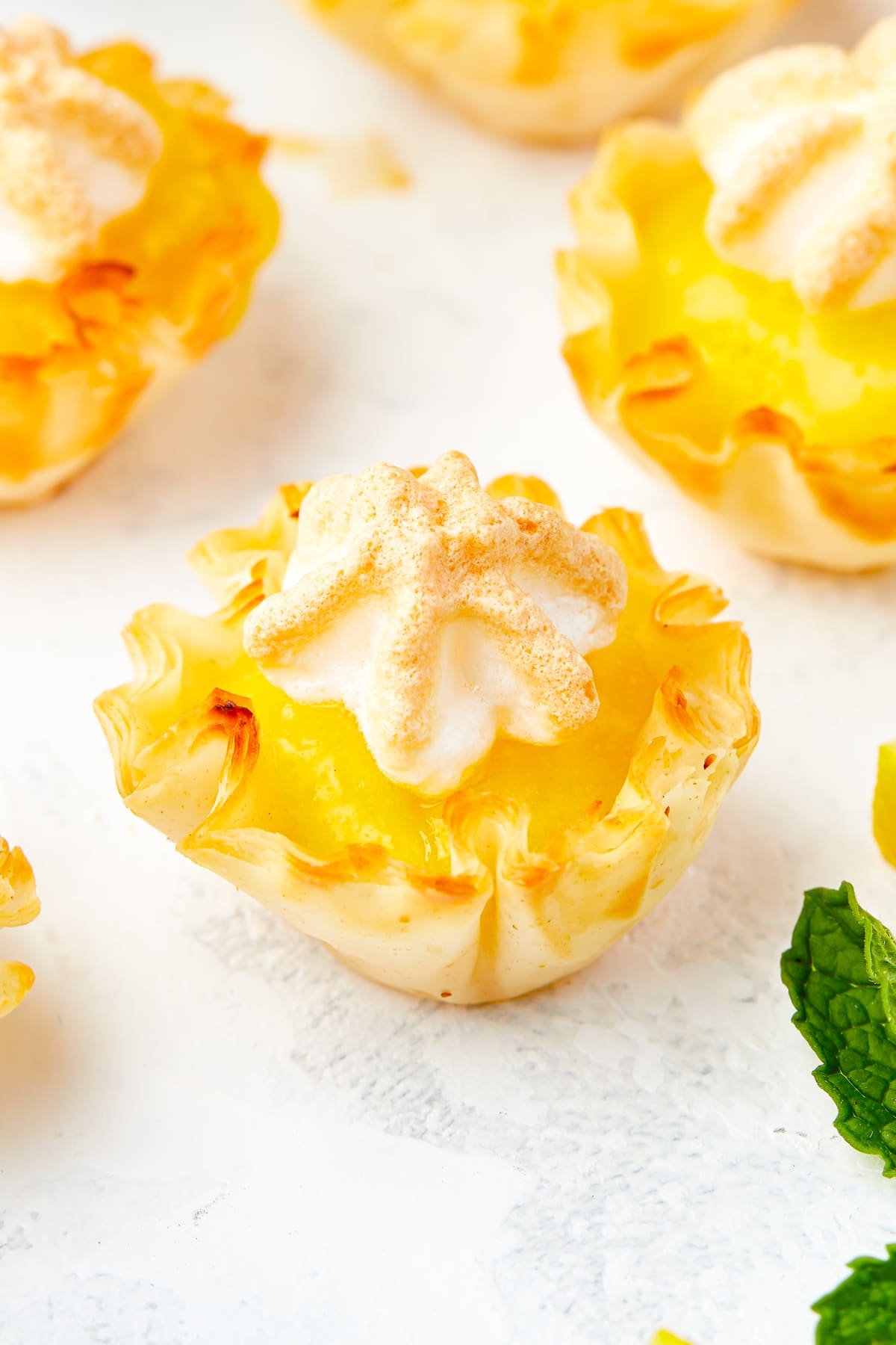 Up close image of mini lemon meringue pies on a white table top