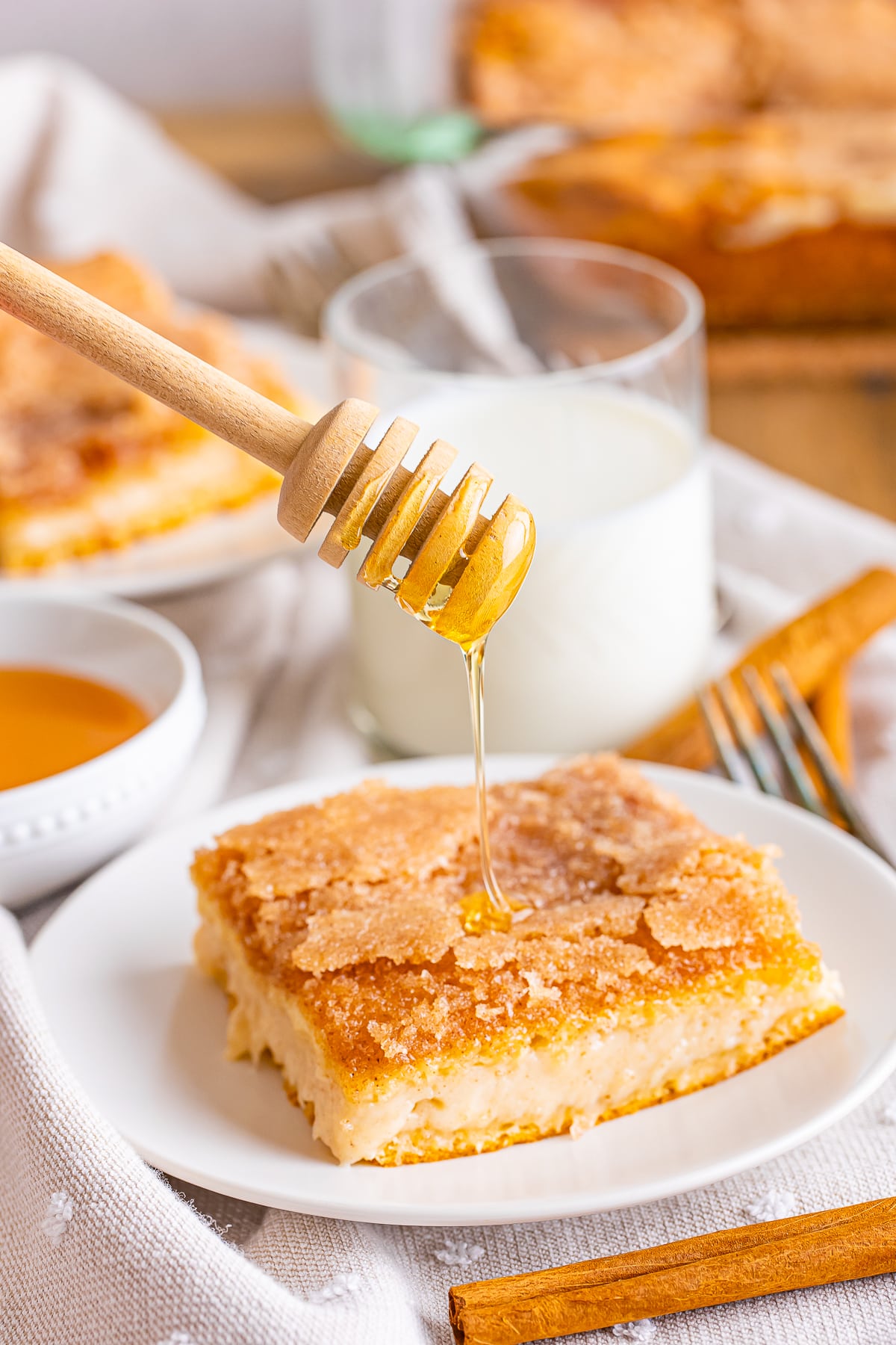 Honey being drizzled on a sopapilla cheesecake bar on a white plate