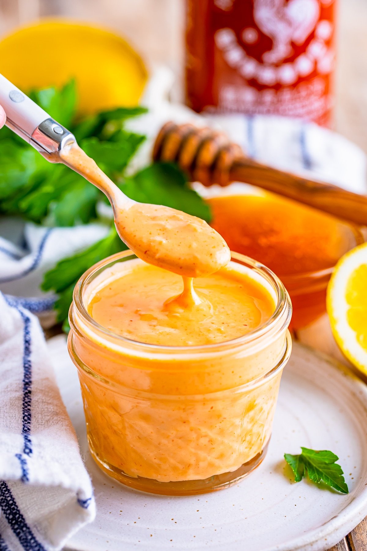 A spoon dipped in sriracha mayo hovering over the mason jar