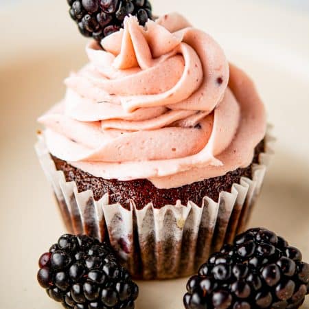Chocolate cupcake piped with blackberry buttercream and topped with a fresh blackberry.