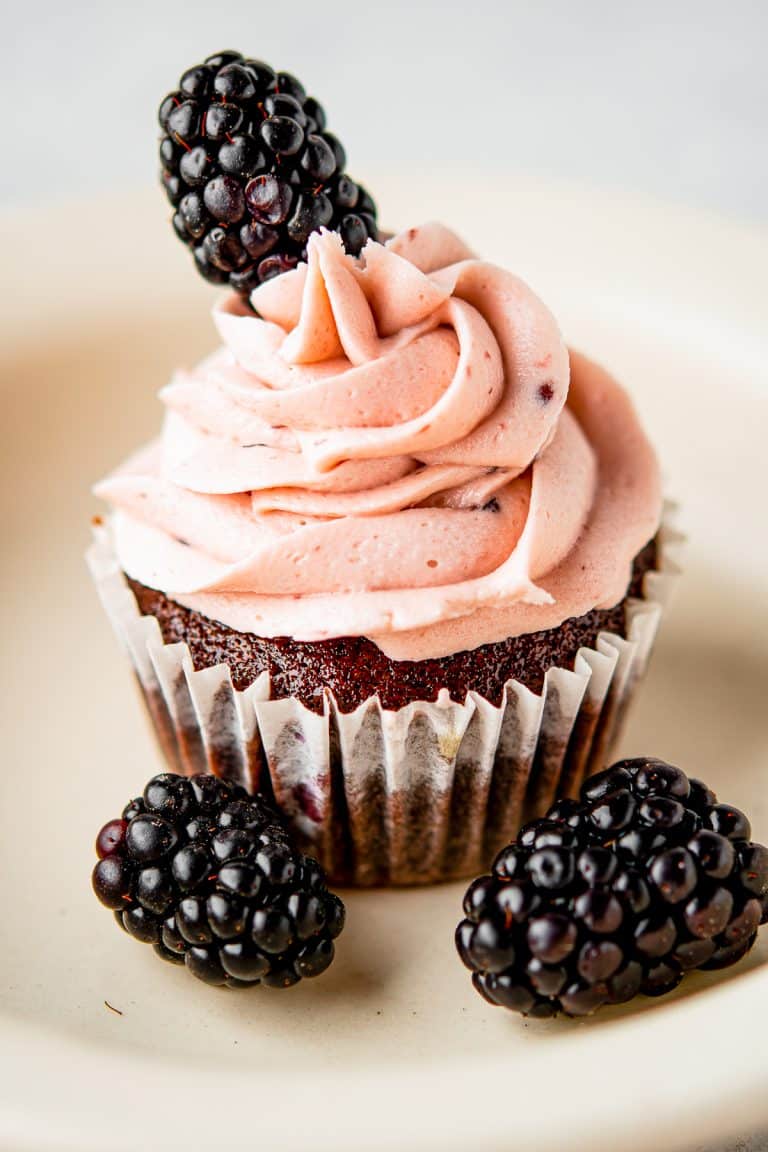 Chocolate cupcake piped with blackberry buttercream and topped with a fresh blackberry.