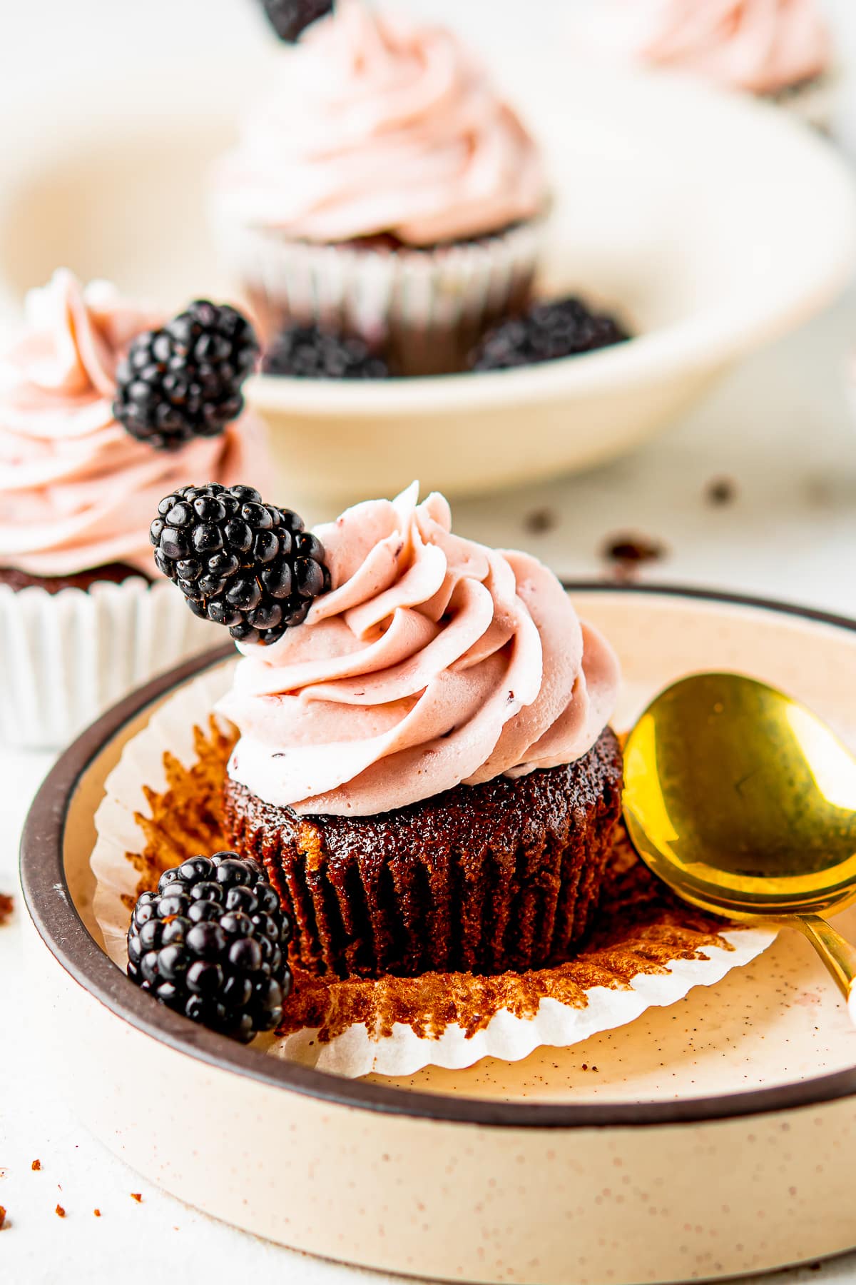chocolate cupcake with blackberry buttercream unwrapped on a tan plate