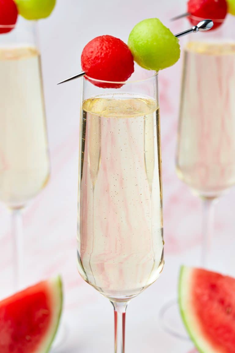 Melon Cocktail in a champagne flute garnished with skewered watermelon and honeydew balls.