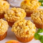 A platter of peach muffins topped with golden streusel crumble.