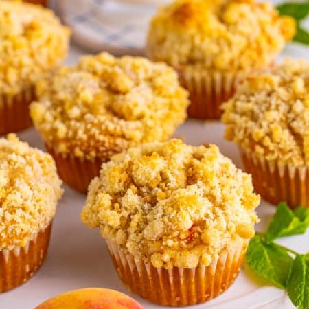 A platter of peach muffins topped with golden streusel crumble.