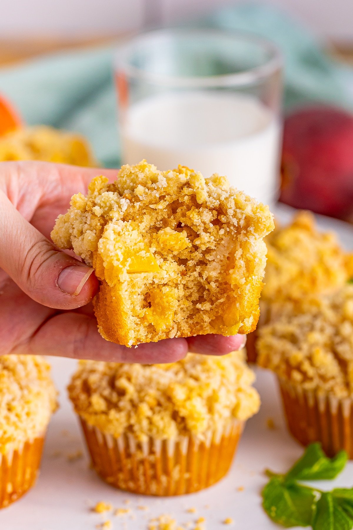 a hand holding a peach muffin with a bite taken out to show the interior