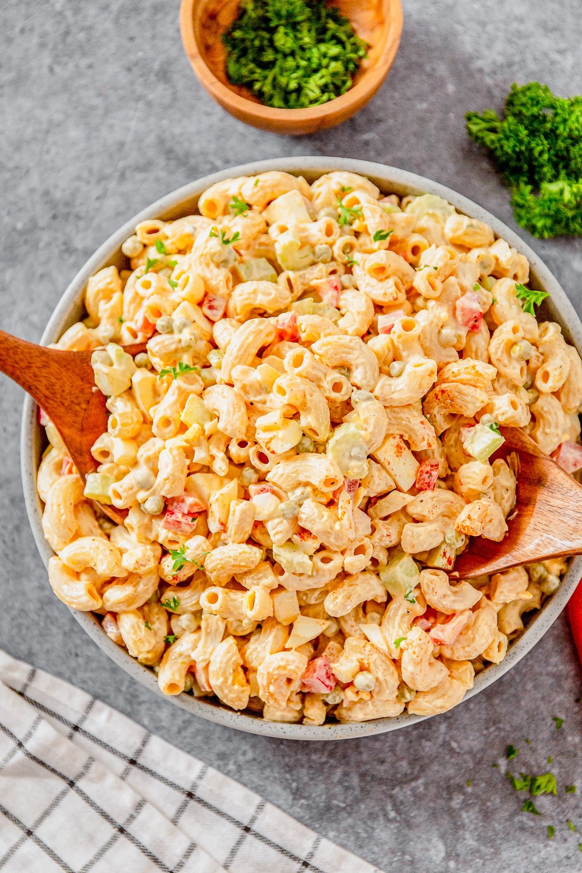 Overhead image of macaroni salad with peas in a grey bowl with serving spoons