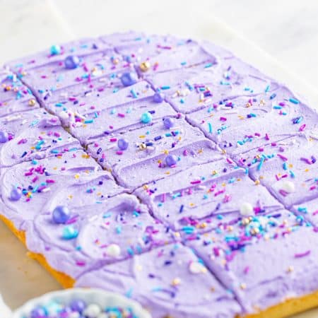 Frosted sugar cookie bars with purple buttercream and sprinkles cut into squares.