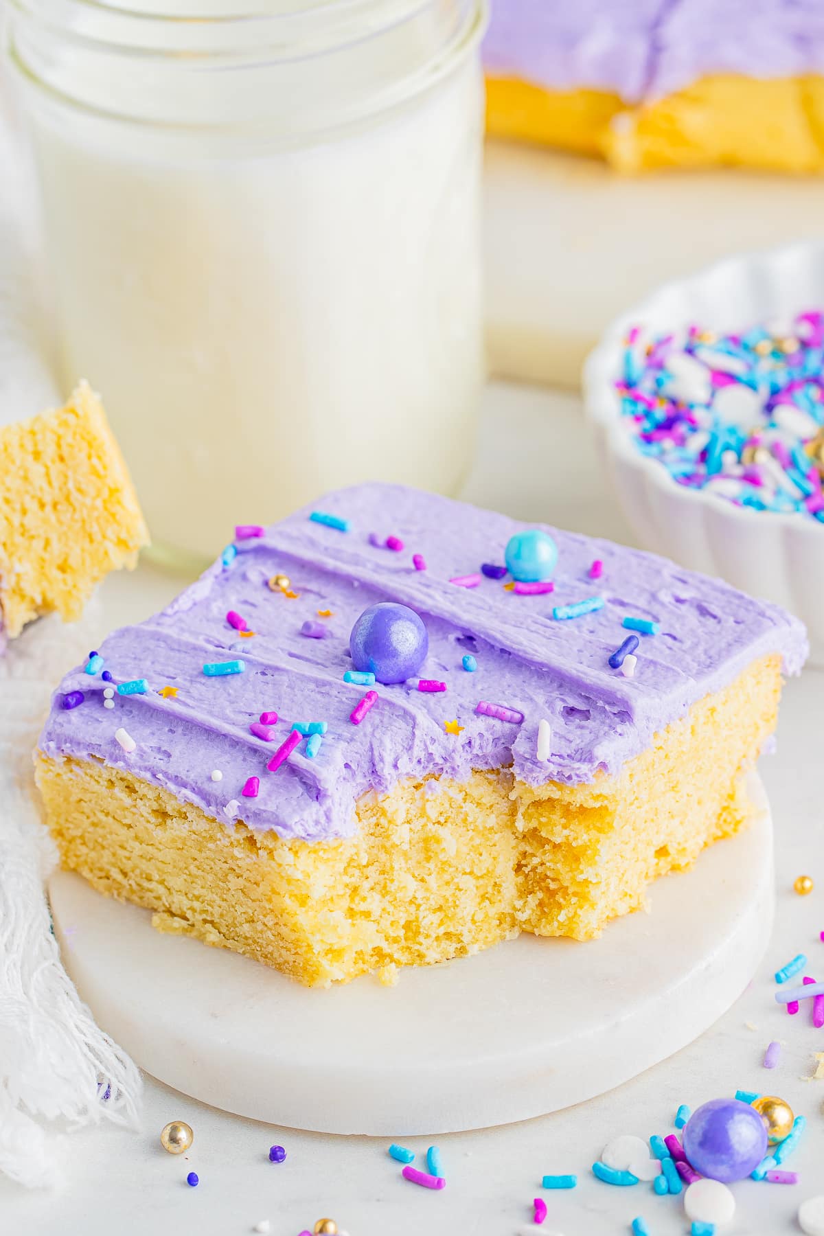 A frosted sugar cookie bar with a bite taken out on a small marble plate
