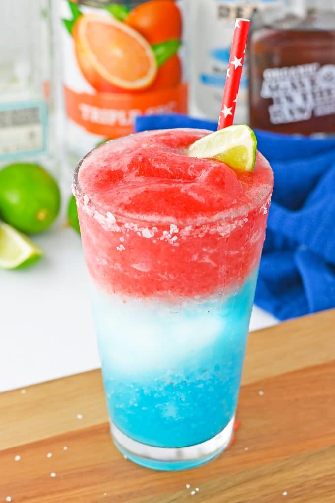 A layered red white and blue 4th of July margarita cocktail garnished with lime.
