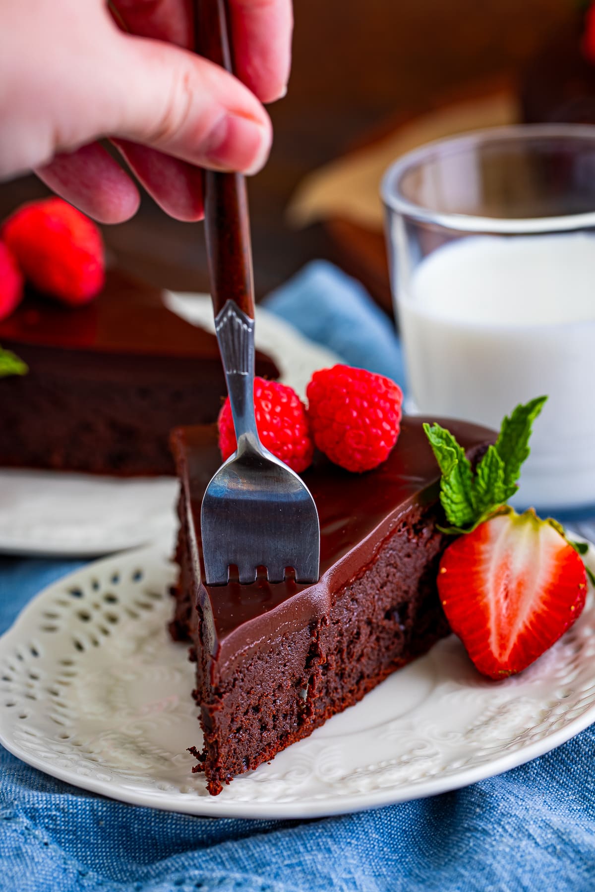 a fork taking a bite out of a slice of flourless chocolate cake recipe on a ivory plate