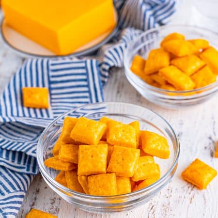 A glass bowl of homemade Cheez-Its with a block of cheddar cheese.