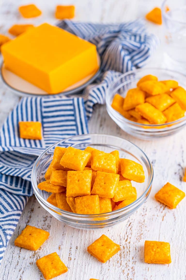 A glass bowl of homemade Cheez-Its with a block of cheddar cheese.