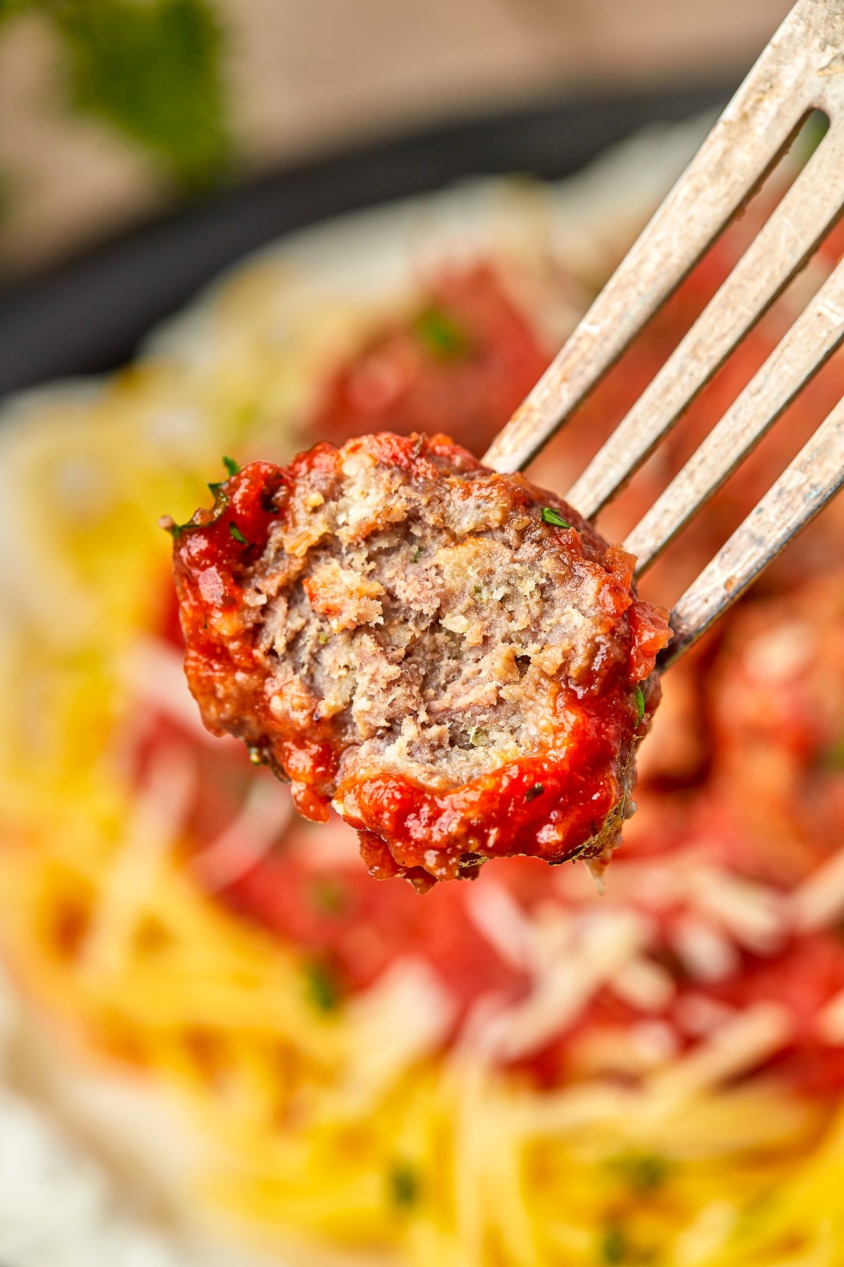 a fork holding up a baked meatball with a bite taken out