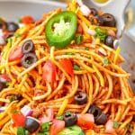 A plate of cheesy taco pasta topped with sour cream, jalapeno, black olives, and cilantro.