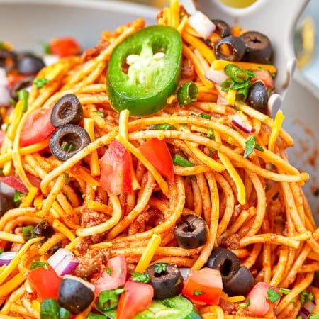 A plate of cheesy taco pasta topped with sour cream, jalapeno, black olives, and cilantro.