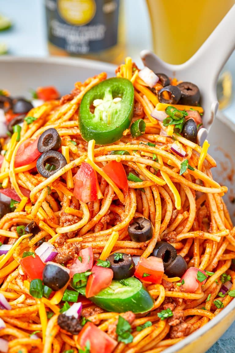 A plate of cheesy taco pasta topped with sour cream, jalapeno, black olives, and cilantro.