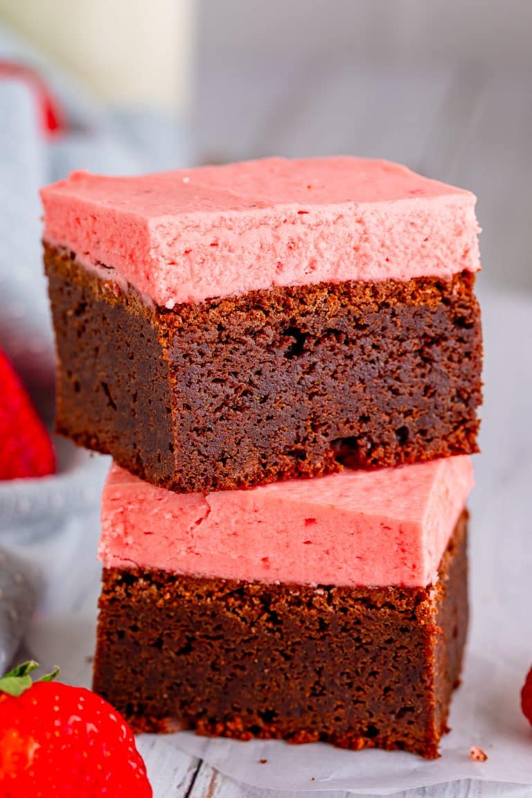 Two frosted brownies stacked to show the fudgy chocolate base and thick strawberry frosting.