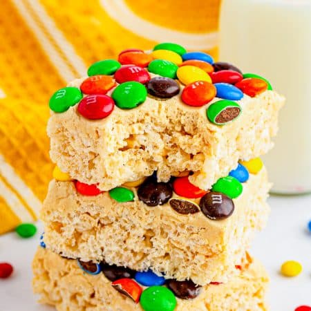 Stacked M&M rice krispie treats with peanut butter frosting and colorful candy.