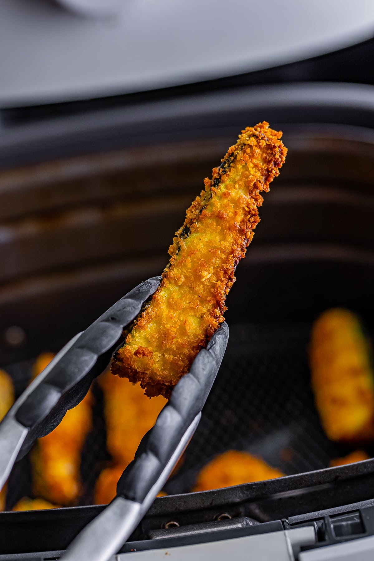 a tongs holding up 1 air fryer zucchini fries in air
