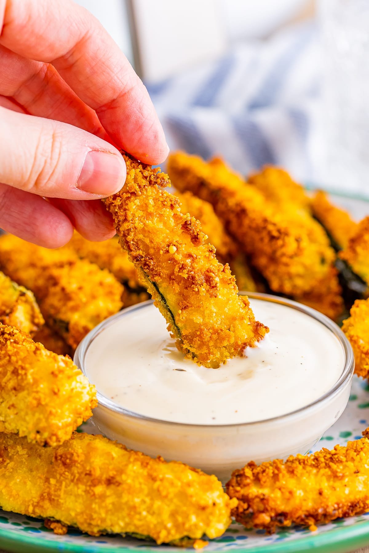 a hand dipping air fryer zucchini fries into dipping sauce