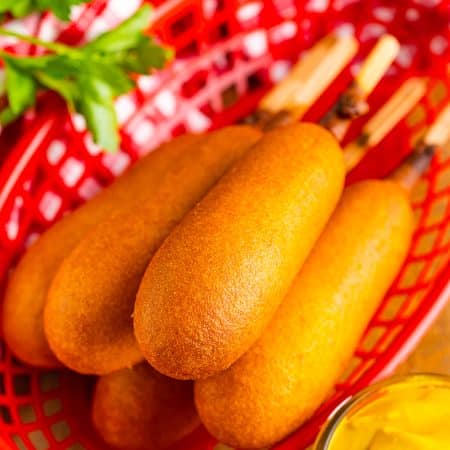 Stack of golden Air Fryer Frozen Corn Dogs on a plate with mustard and ketchup ready to serve.