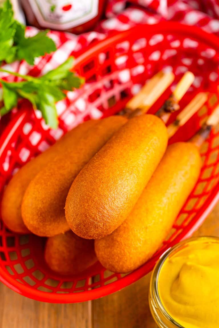 Stack of golden Air Fryer Frozen Corn Dogs on a plate with mustard and ketchup ready to serve.