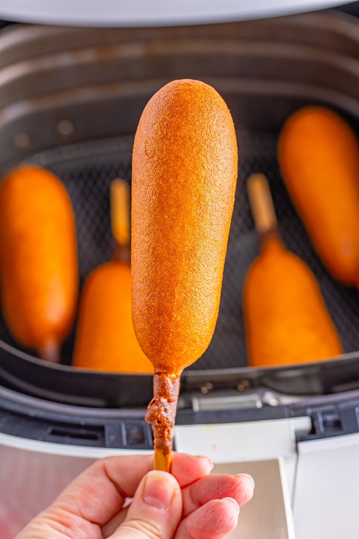 a hand holding up a cooked air fryer frozen corn dog