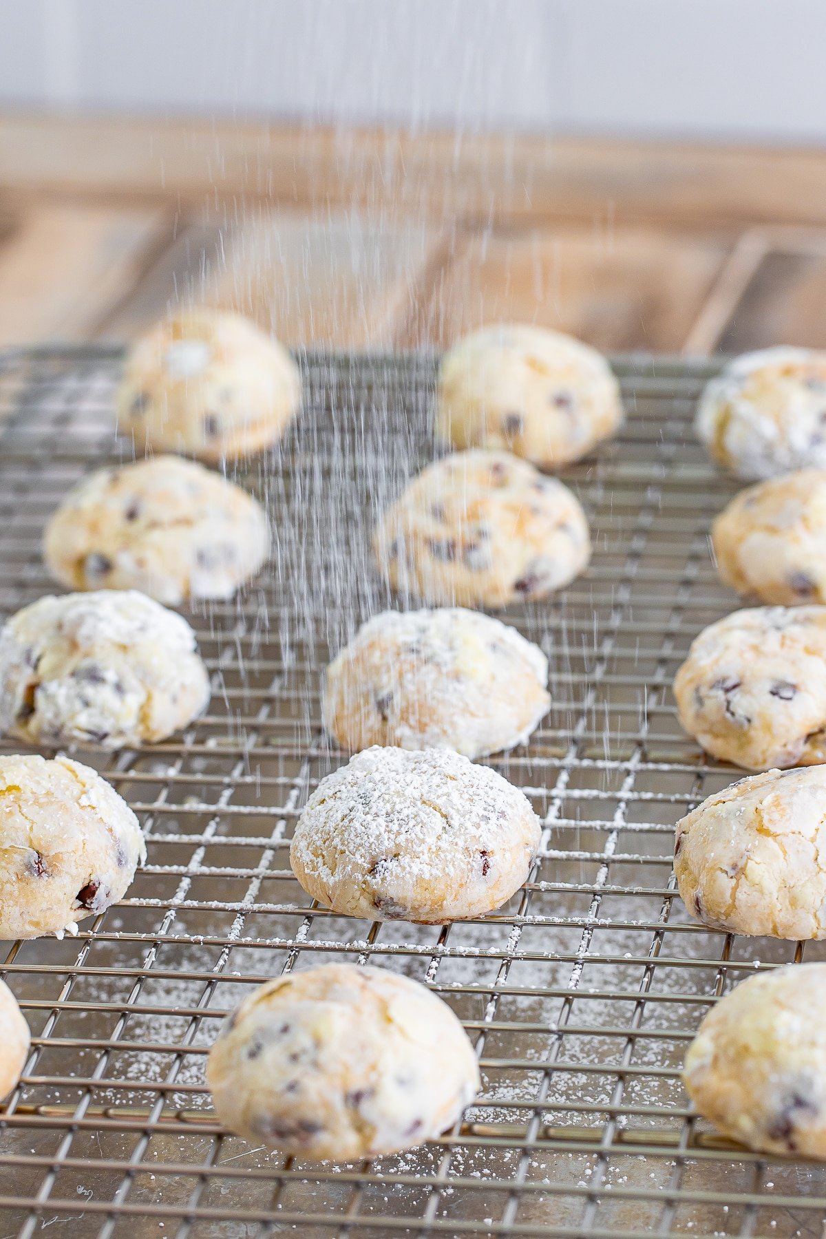 chocolate chip cream cheese cookie on a wire rack being dusted with powdered sugar