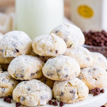 Cream cheese chocolate chip cookies dusted with powdered sugar on a plate with milk.