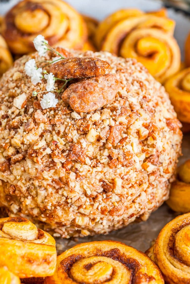A cinnamon cream cheese ball coated in praline pecans on a plate surrounded by cookies and graham crackers for dipping.