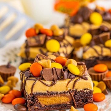 Stacked peanut butter brownies topped with peanut butter frosting and Reeses pieces.