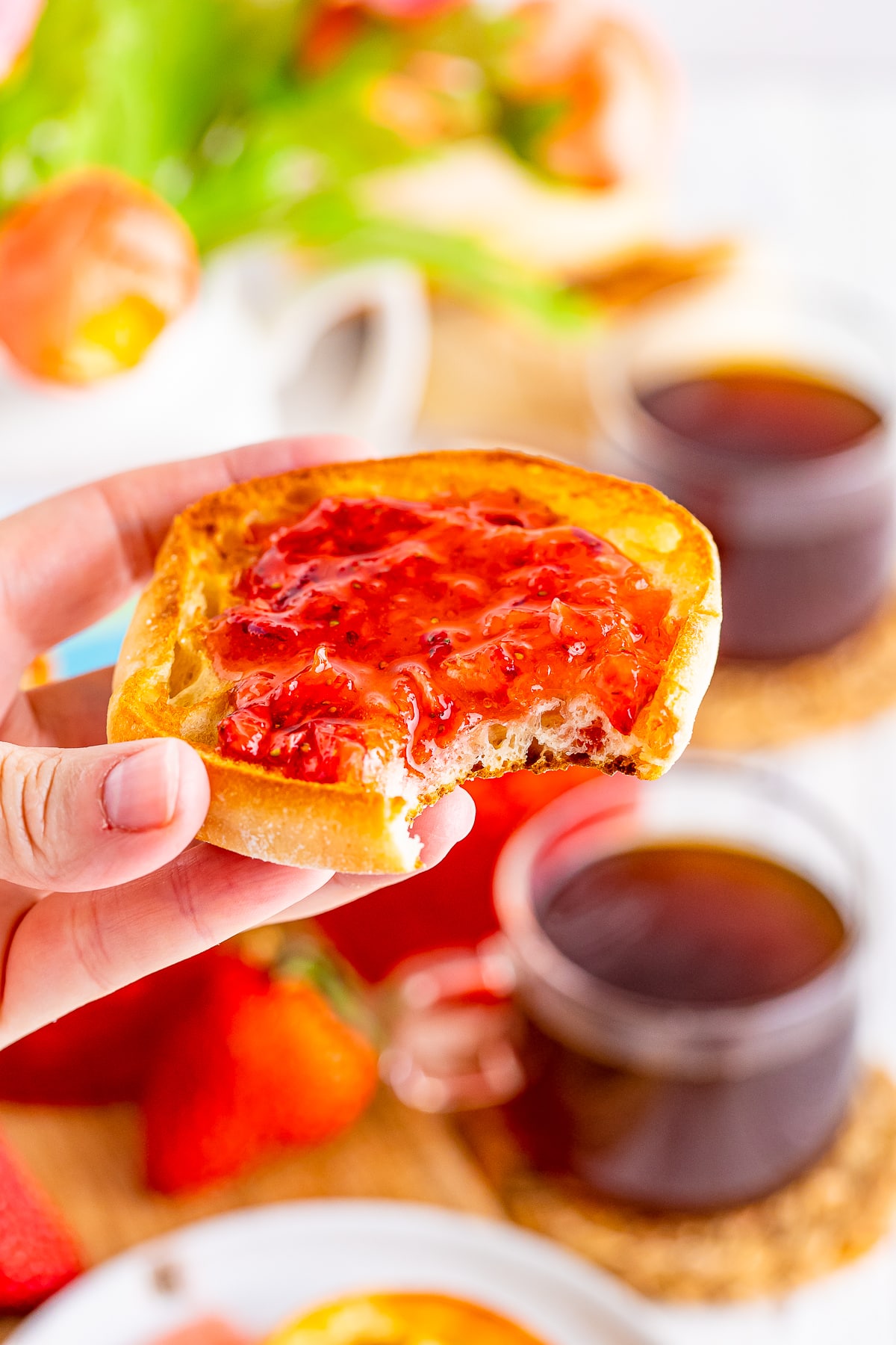 a hand holding an english muffin with strawberry freezer jam with a bite taken out