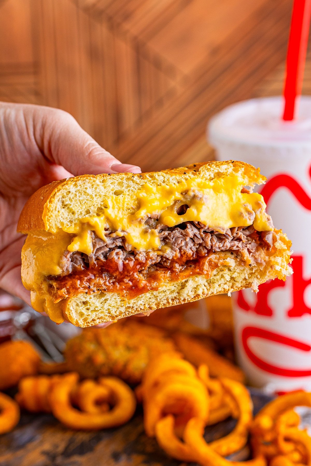 a hand holding up an arbys beef and cheddar in air that is cut in half