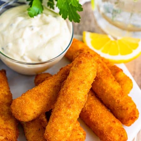 Crispy air fryer fish sticks on a plate with tartar sauce and lemon wedges.