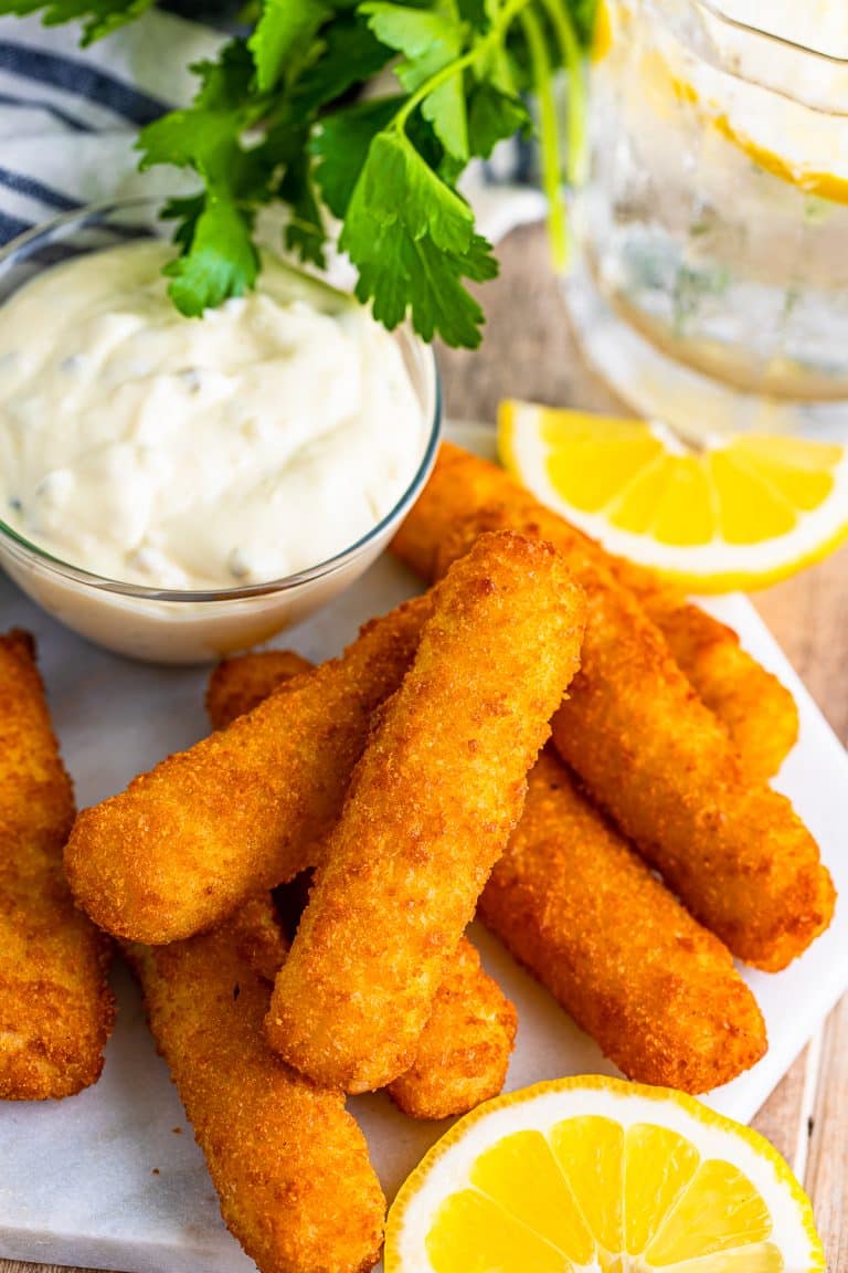 Crispy air fryer fish sticks on a plate with tartar sauce and lemon wedges.